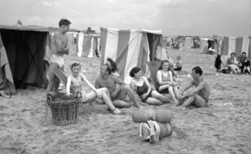 Young people sat around beach huts in 1950